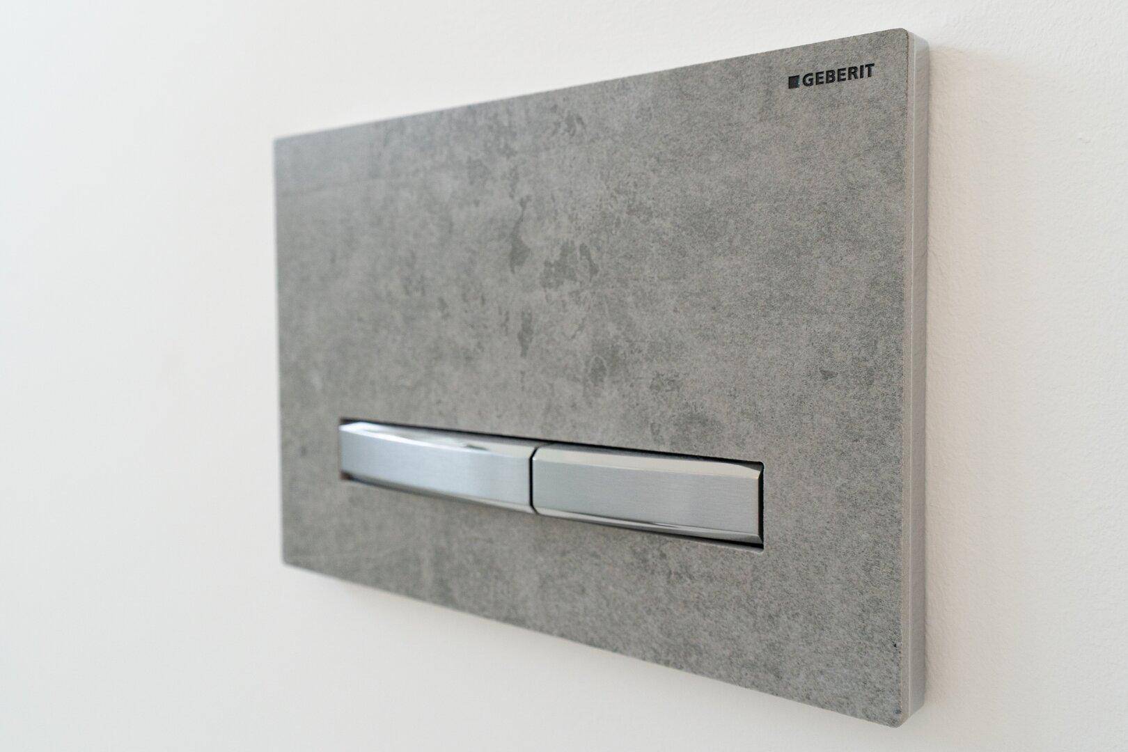 Detailaufnahme einer modernen Toilettenspülung mit grauer Steinoptik und Chrom-Elementen.