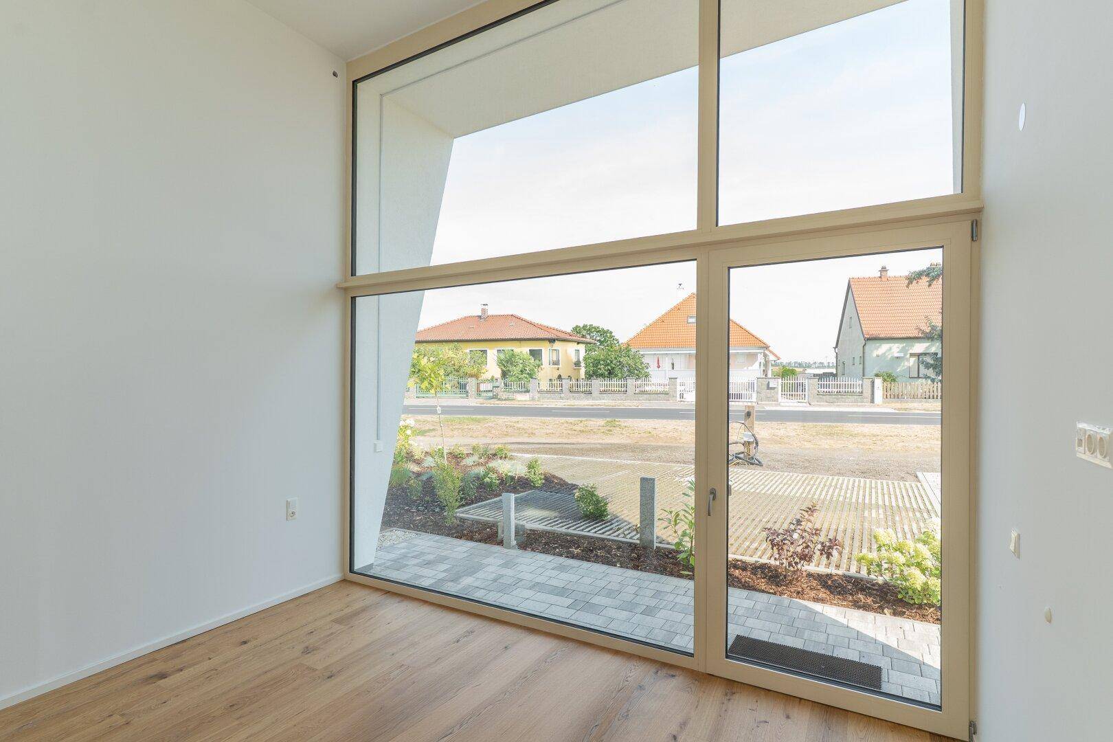 Heller Raum mit großen Fenstern, Holzboden und Blick auf die Straße und Nachbarhäuser.