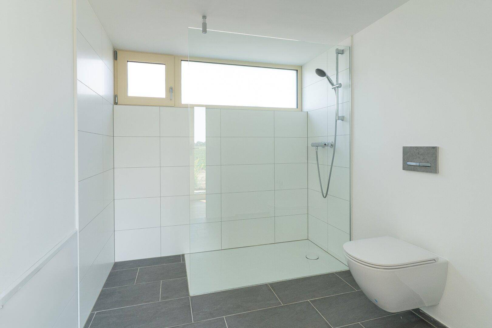 Modernes Badezimmer mit begehbarer Dusche, wandhängendem WC und Fenster.