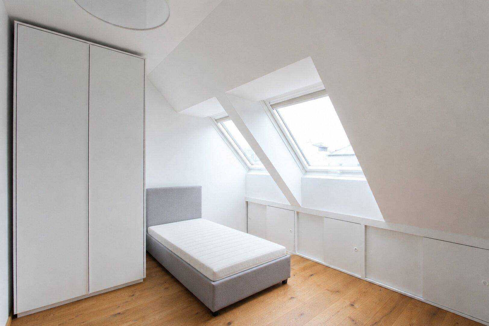 Helles Schlafzimmer im Dachgeschoss mit Holzboden, Dachfenstern und integrierten Stauräumen.