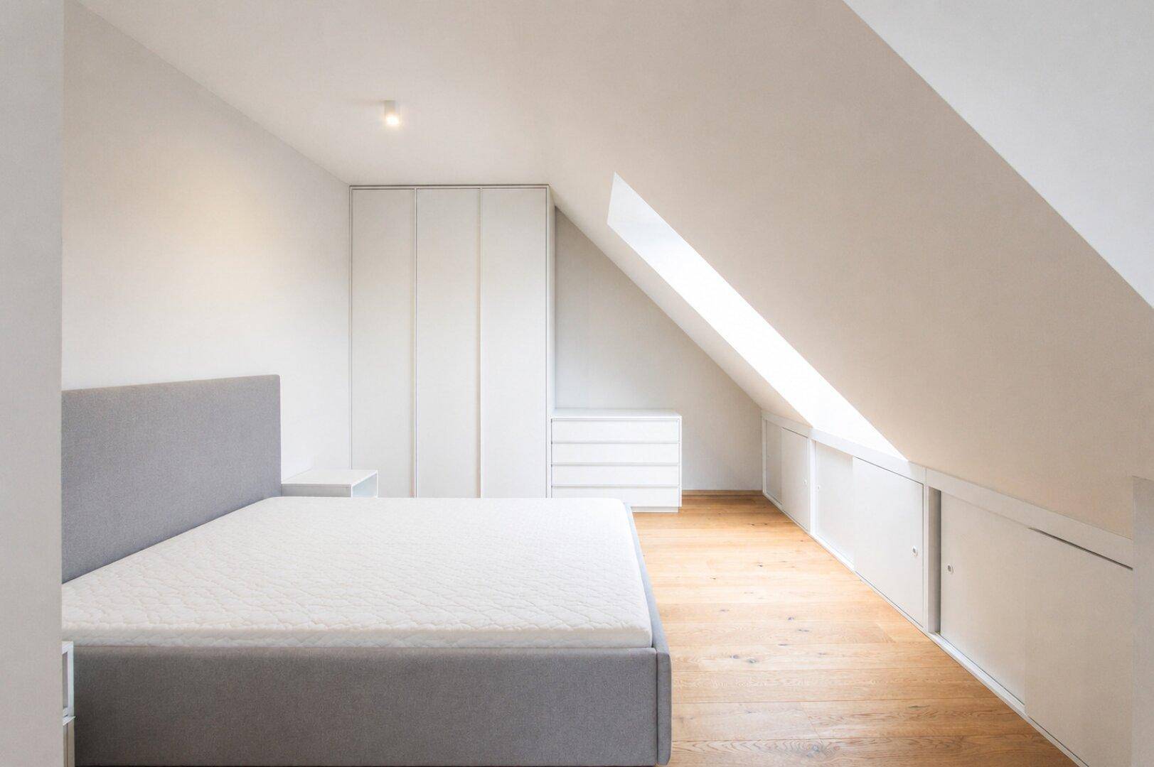 Geräumiges Dachgeschoss-Schlafzimmer mit modernem Bett, Holzboden und viel natürlichem Licht.