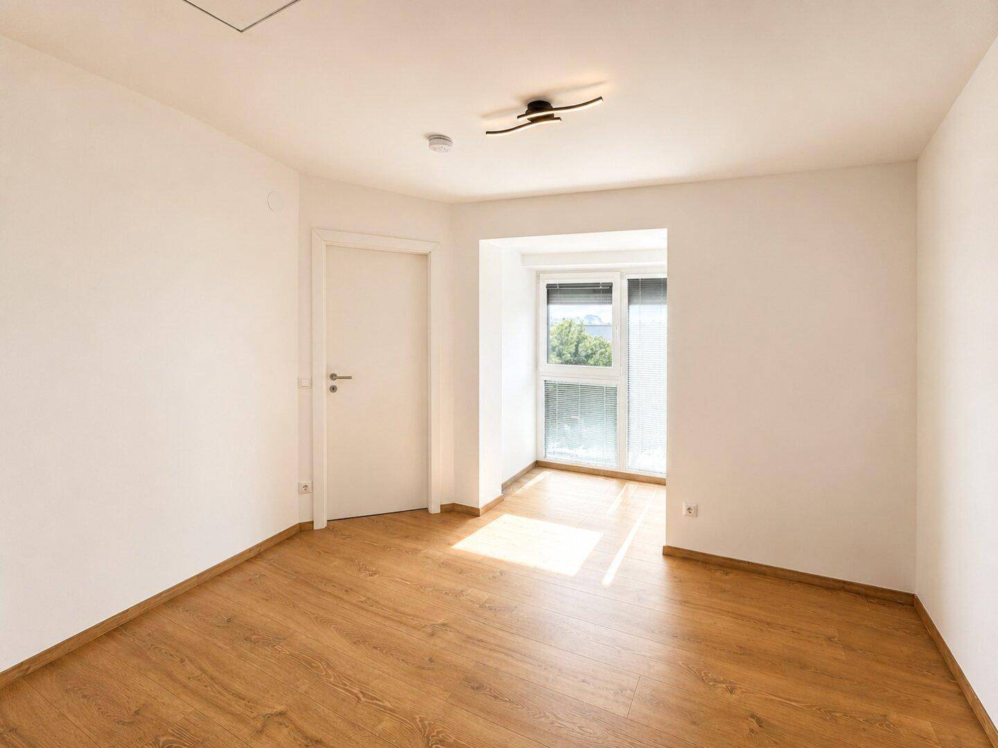 Helles Zimmer mit Laminatboden und großem Fenster, bereit zur individuellen Gestaltung.