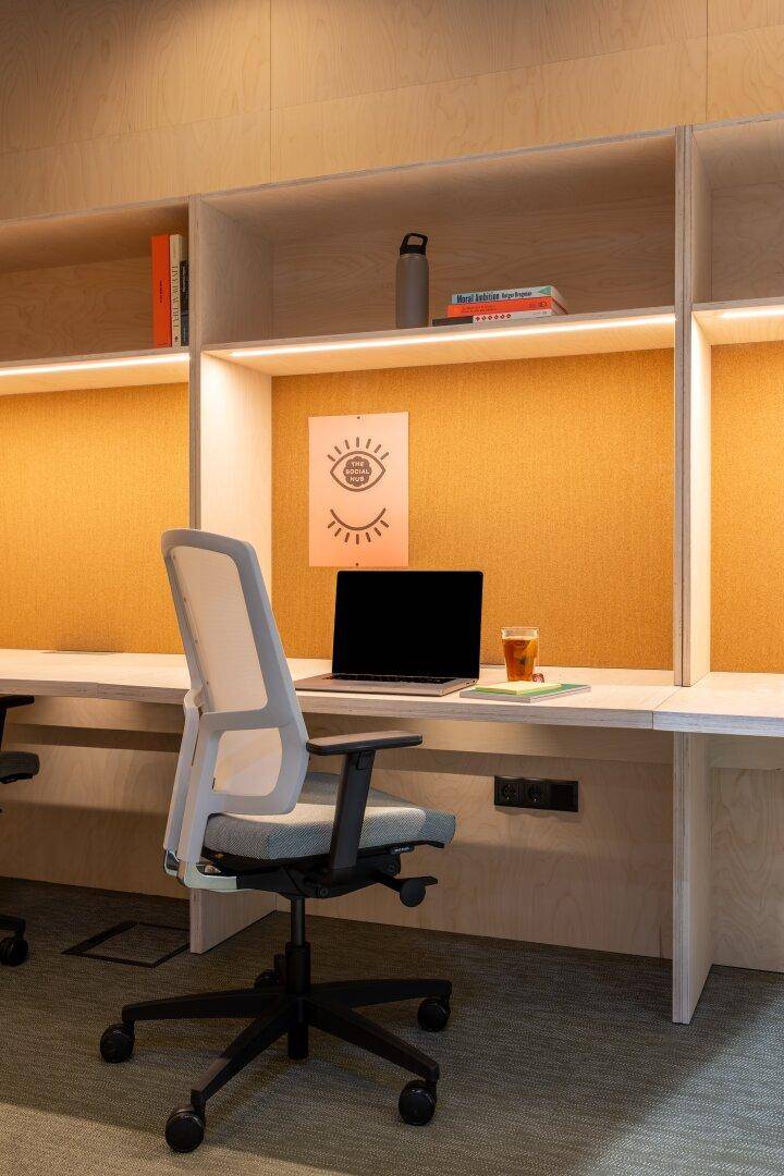 Individueller Arbeitsplatz in einem modernen Büro mit Laptop, ergonomischem Stuhl und integrierten Regalen.