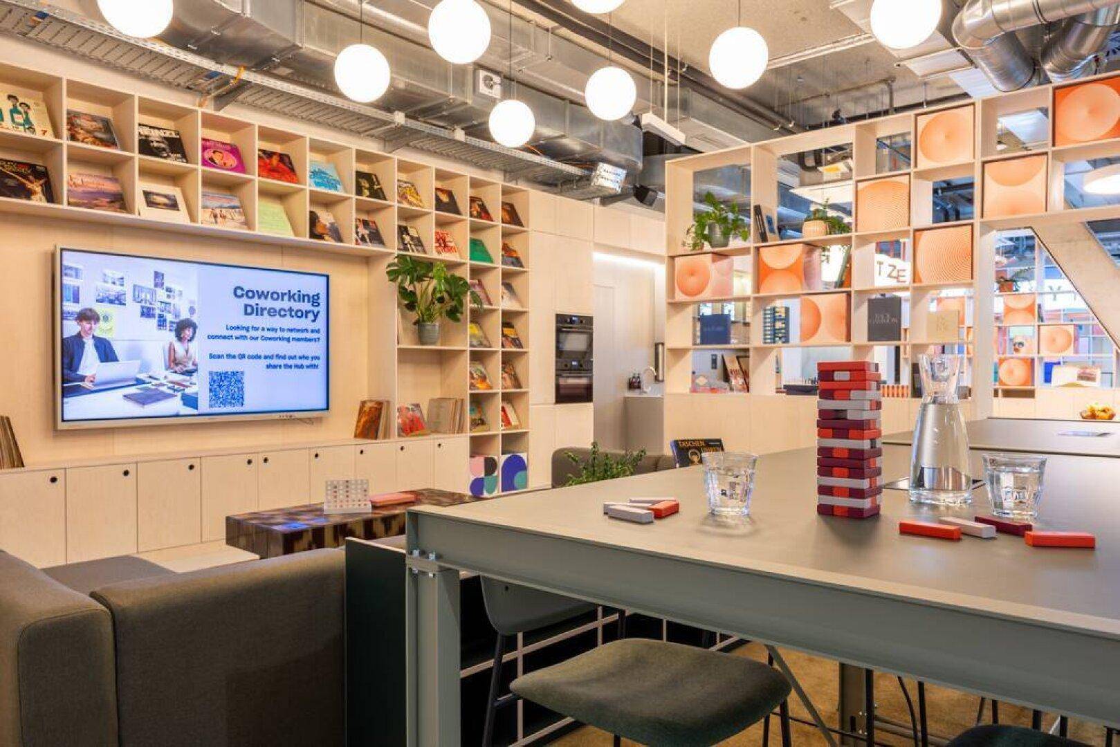 Gemütlicher Loungebereich in einem Coworking Space mit Bücherregalen, Fernseher und einer hohen Theke.
