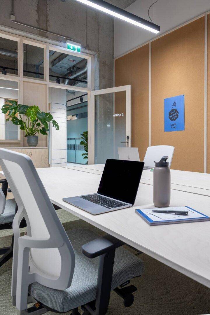 Heller Besprechungsraum mit langem Tisch, modernen Stühlen und Laptops, umgeben von Glaswänden.