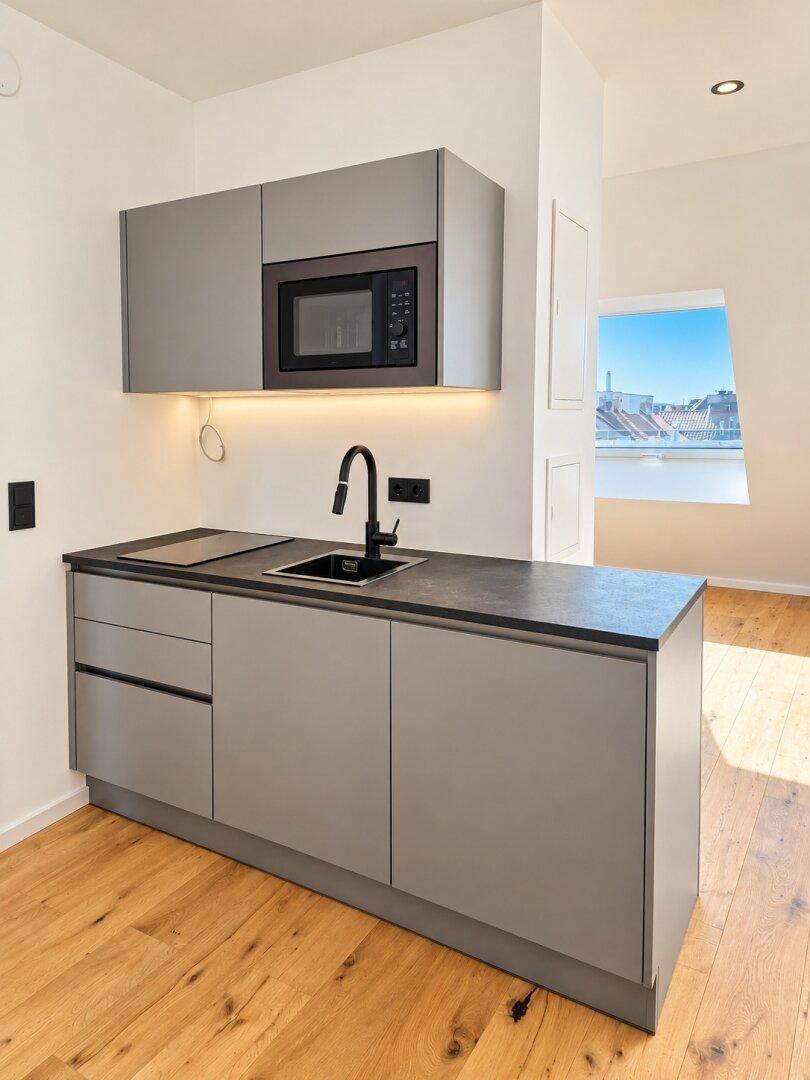 Moderne Küchenzeile im Dachgeschoss mit grauen Schränken, integrierter Mikrowelle und Holzboden.