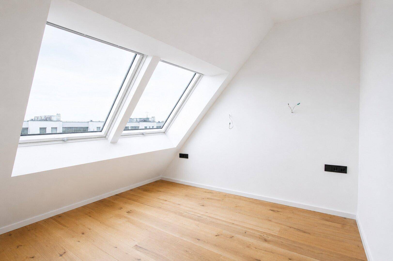 Geräumiges Dachgeschosszimmer mit hellem Holzboden und großen Dachfenstern, bereit zur Einrichtung.