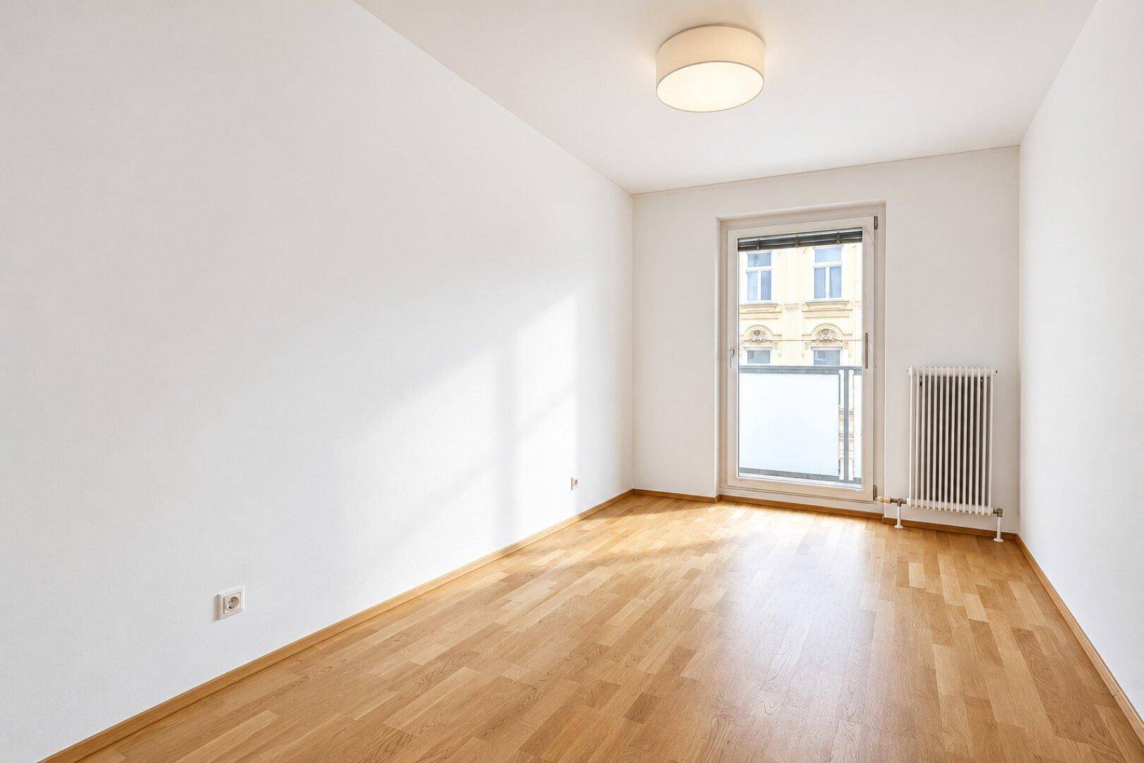 Heller Raum mit Parkettboden und Zugang zu einem Balkon, ideal als Schlafzimmer.