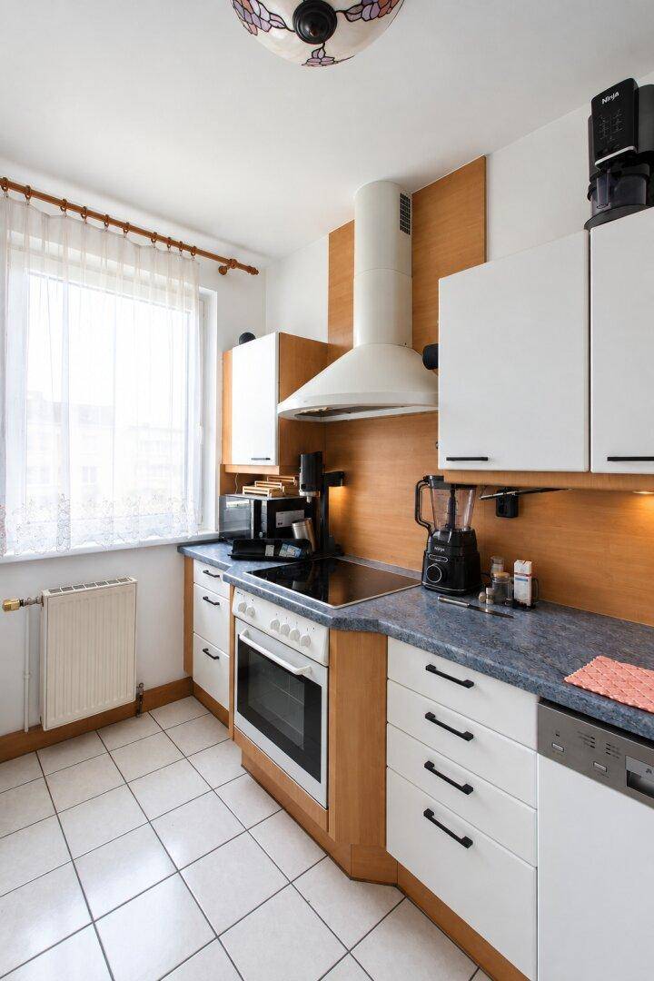 Funktionale Küche mit weißen Schränken, Holzdetails und modernen Geräten, inklusive Fenster.