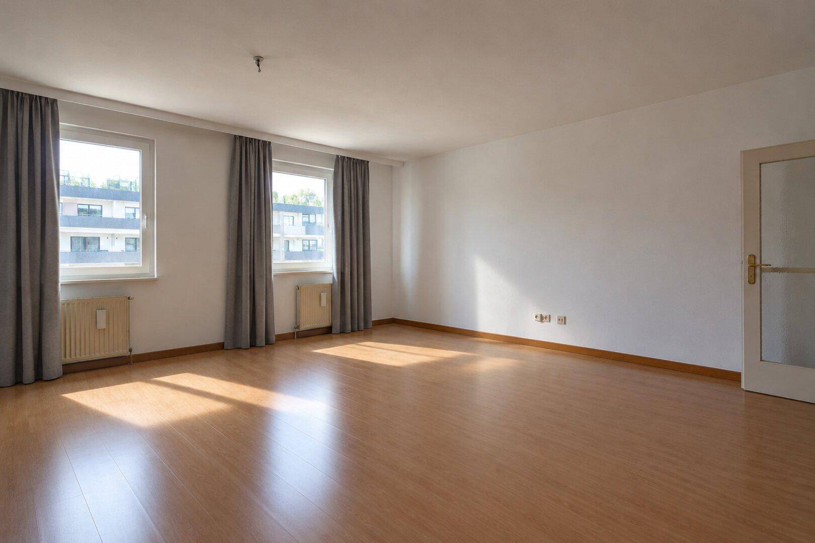 Geräumiges, unmöbliertes Wohnzimmer mit Laminatboden und hellen Wänden, bereit zum Einzug.