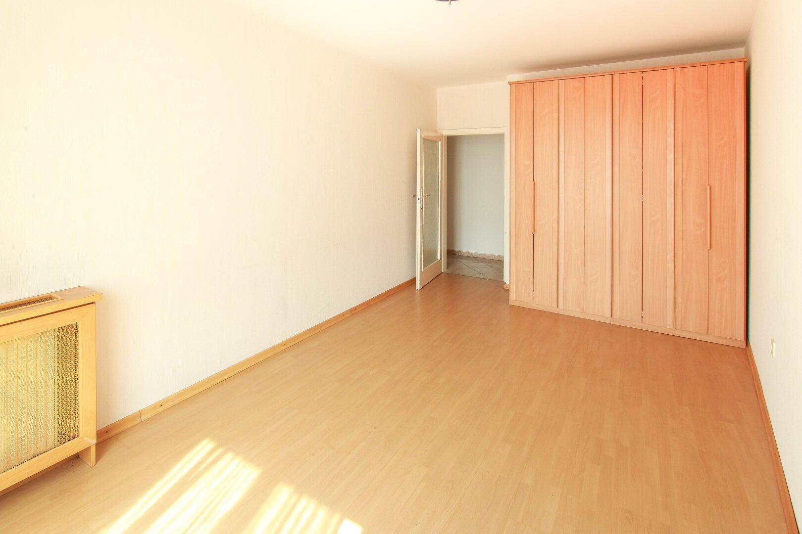 Schlafzimmer mit Laminatboden und einem großen Holzschrank, der viel Stauraum bietet.