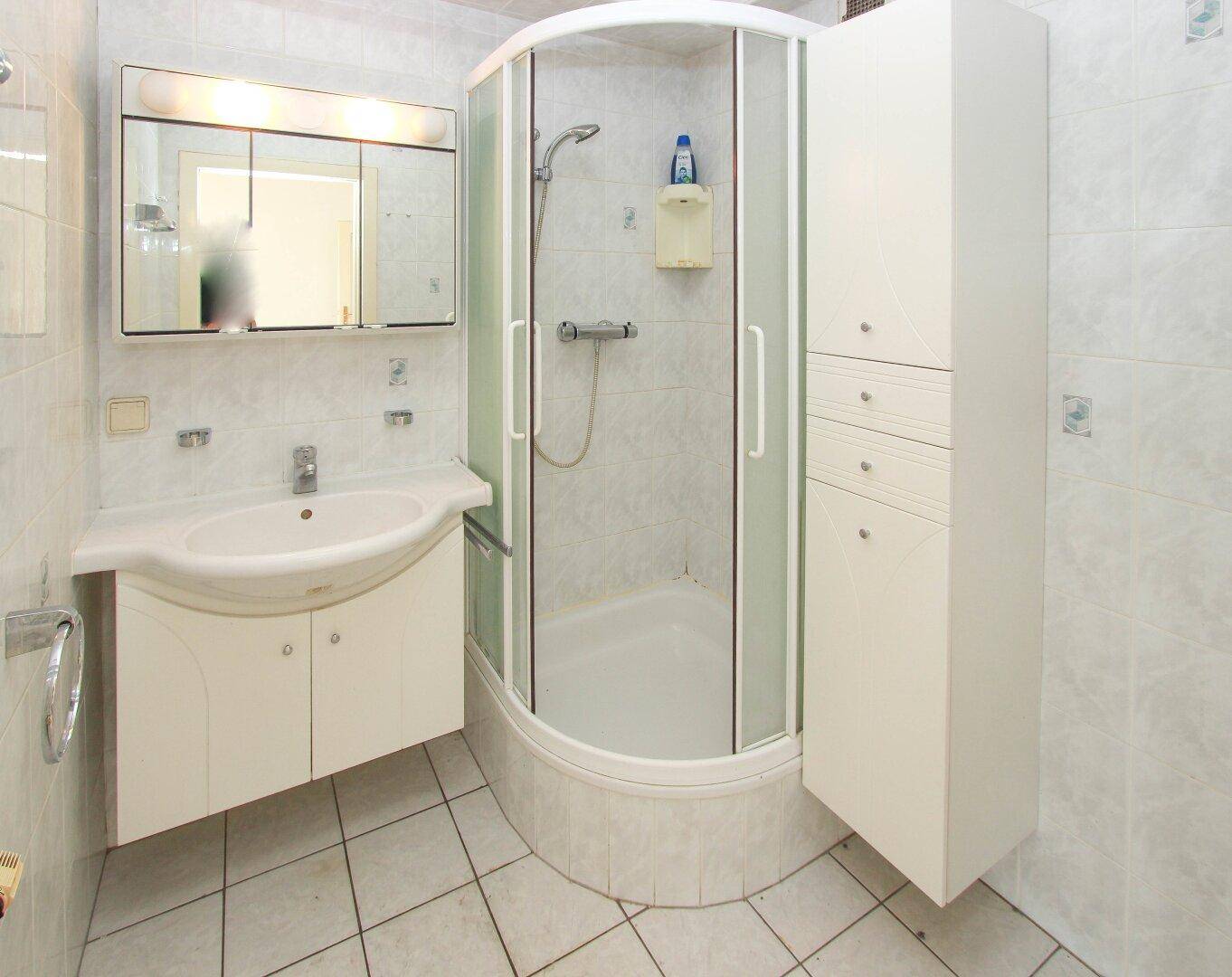Modernes Badezimmer mit Duschkabine, Waschbecken und Spiegelschrank, hell gefliest.