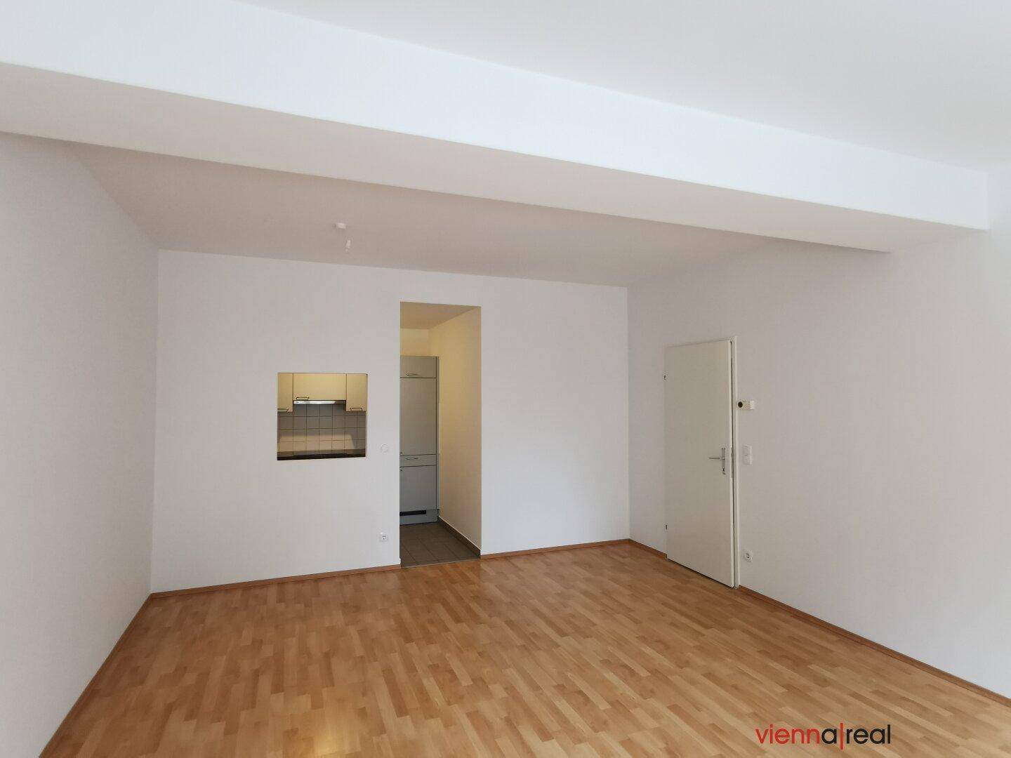 Geräumiger Wohnbereich mit hellem Parkettboden und einer Durchreiche zur Küche, bietet viel Gestaltungspotenzial.