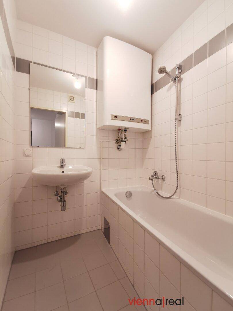 Gefliestes Badezimmer mit Badewanne, Dusche und Waschbecken, ausgestattet mit einem Wandspiegel und Boiler.
