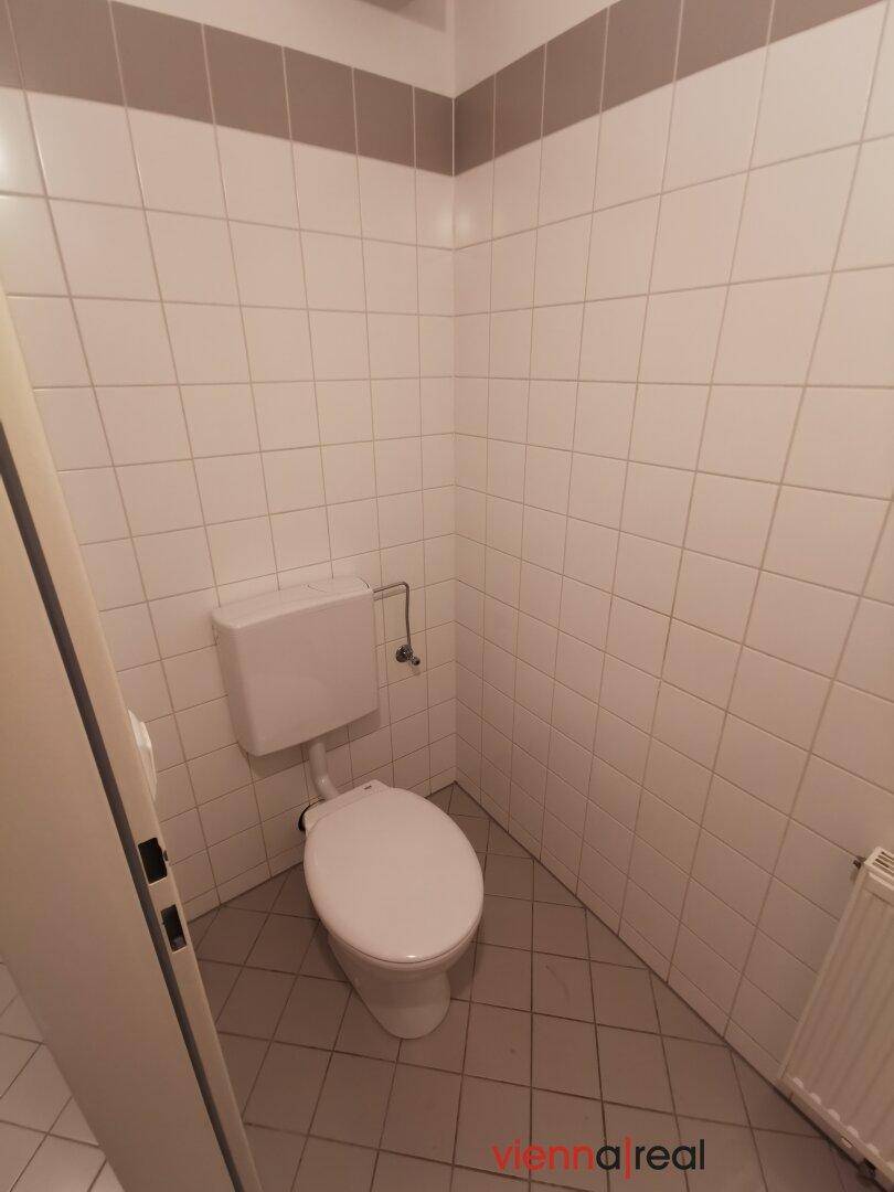 Separate Toilette mit Wandfliesen und einem einfachen WC, sauber und funktional gestaltet.