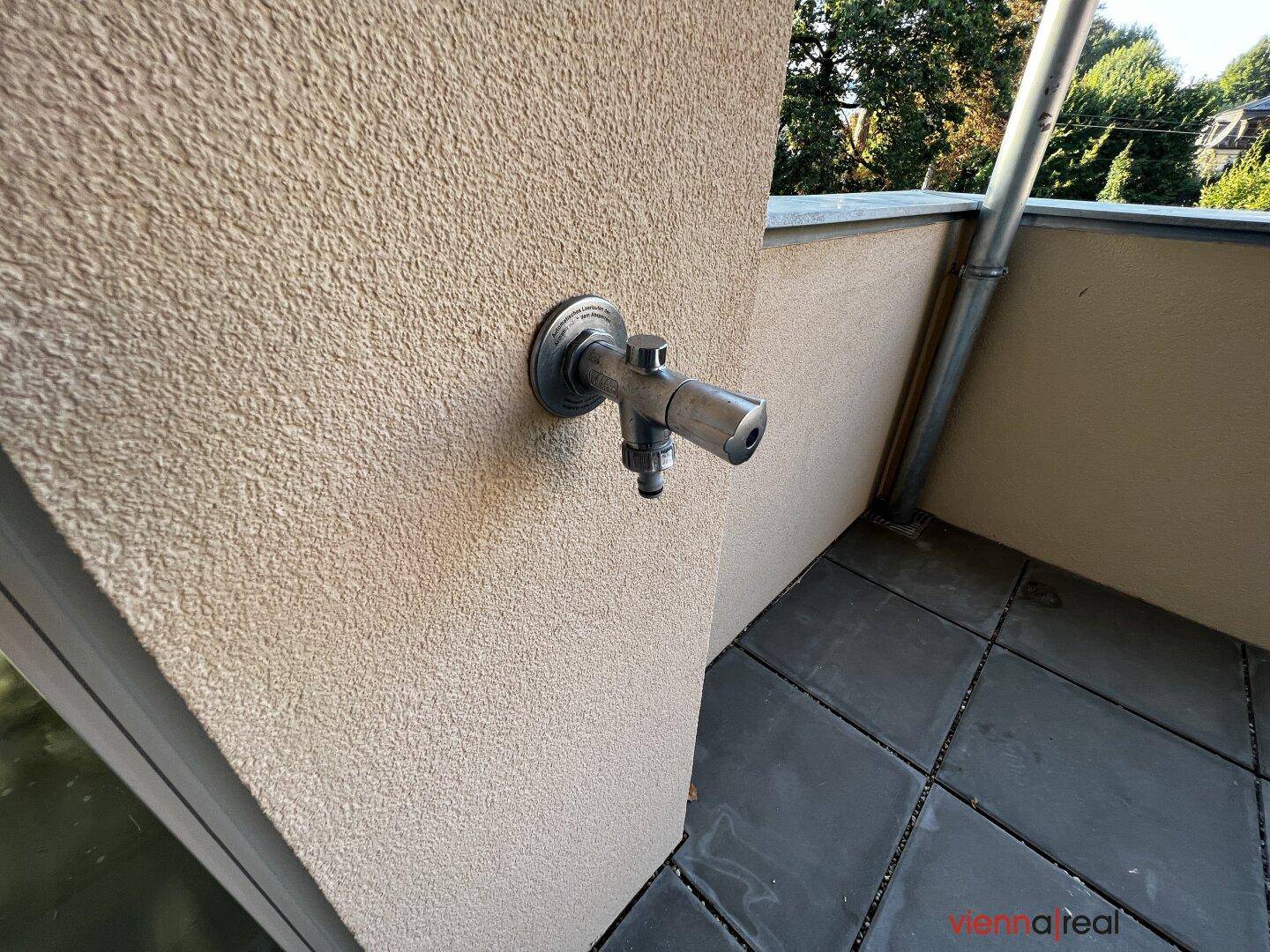 Detailaufnahme eines Wasserhahns an der Balkonwand, praktisch für die Pflanzenbewässerung.