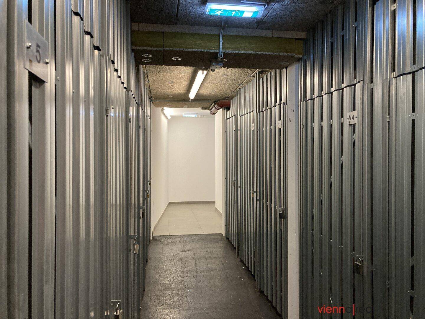 Langer Gang im Kellerbereich mit zahlreichen individuellen Lagerabteilen aus Metall.