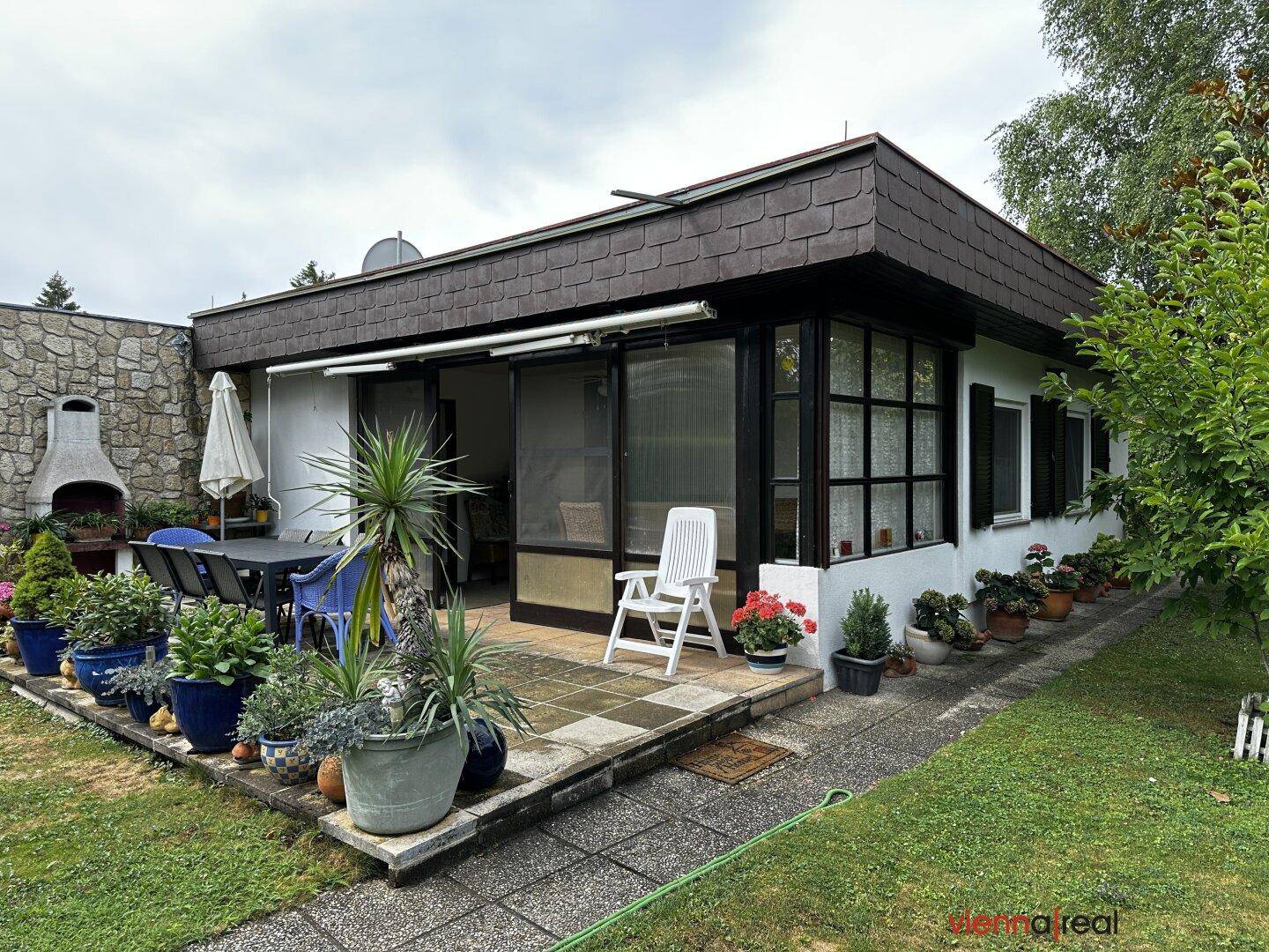 Ansicht des Hauses mit einer großen Terrasse, Steingrill und gepflegtem Gartenbereich.
