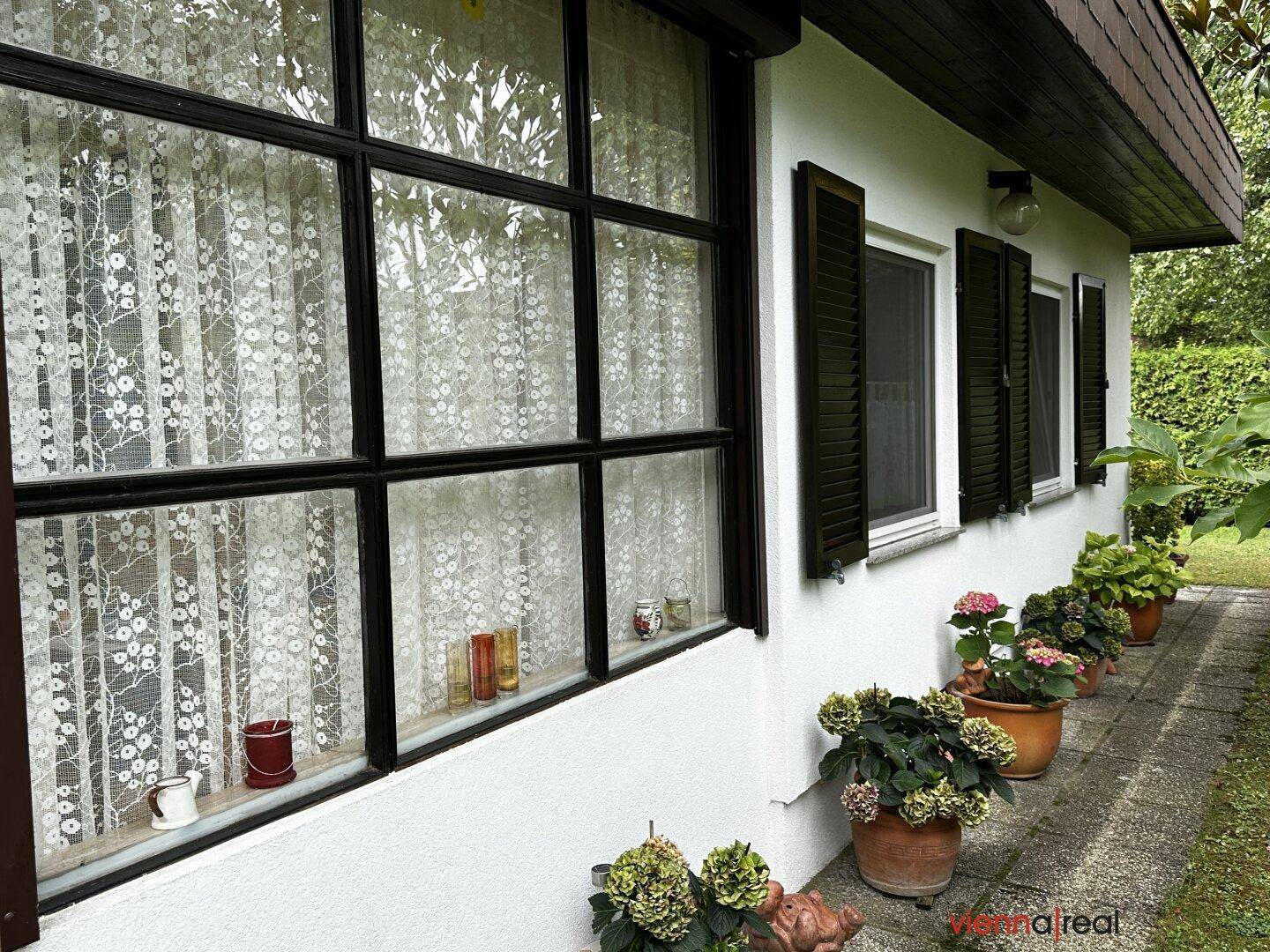 Seitenansicht des Hauses mit Fenstern, Fensterläden und Blumenkübeln entlang des Weges.