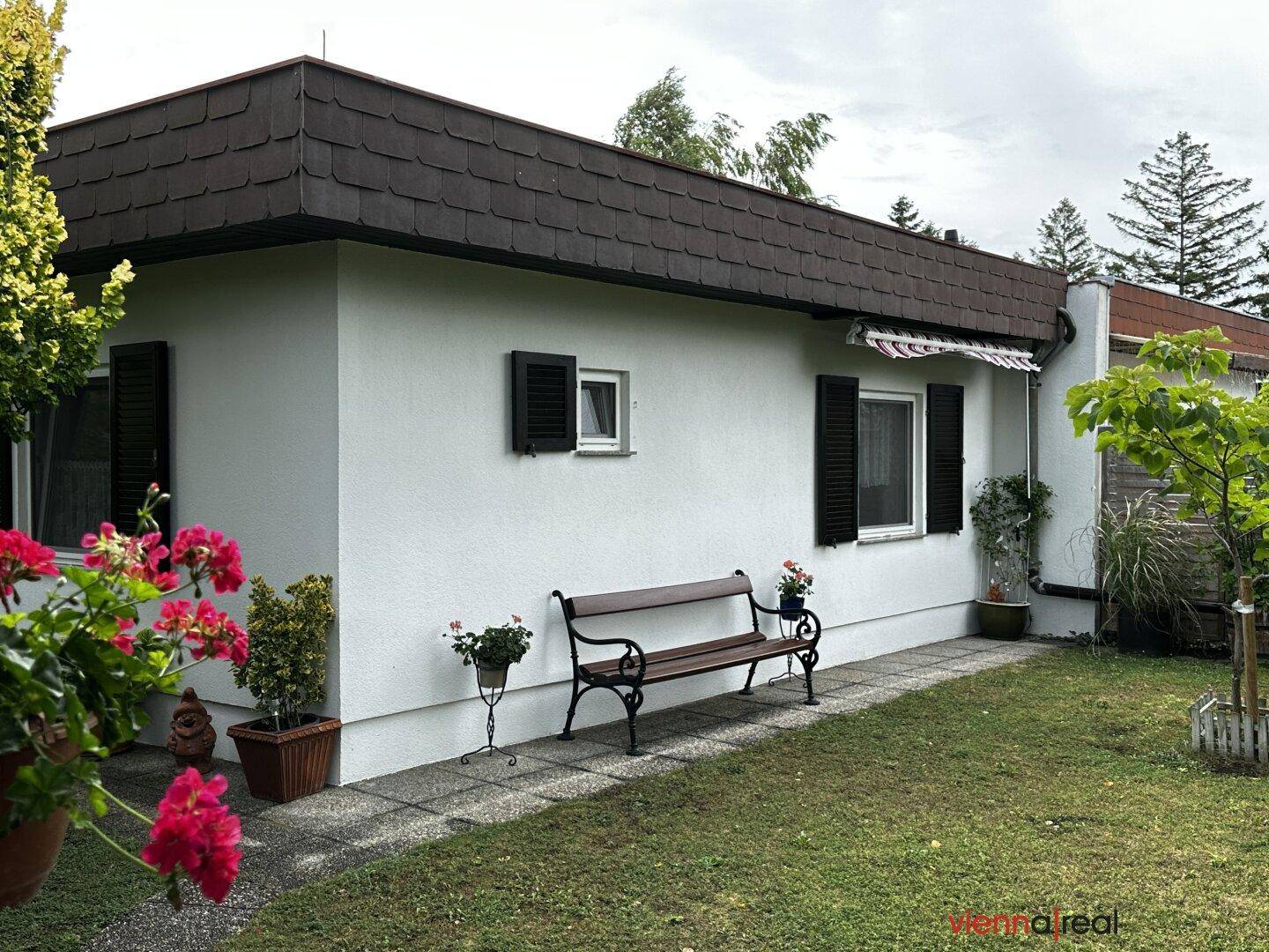 Seitenansicht des Hauses mit einer Gartenbank und gepflegtem Rasen unter bewölktem Himmel.