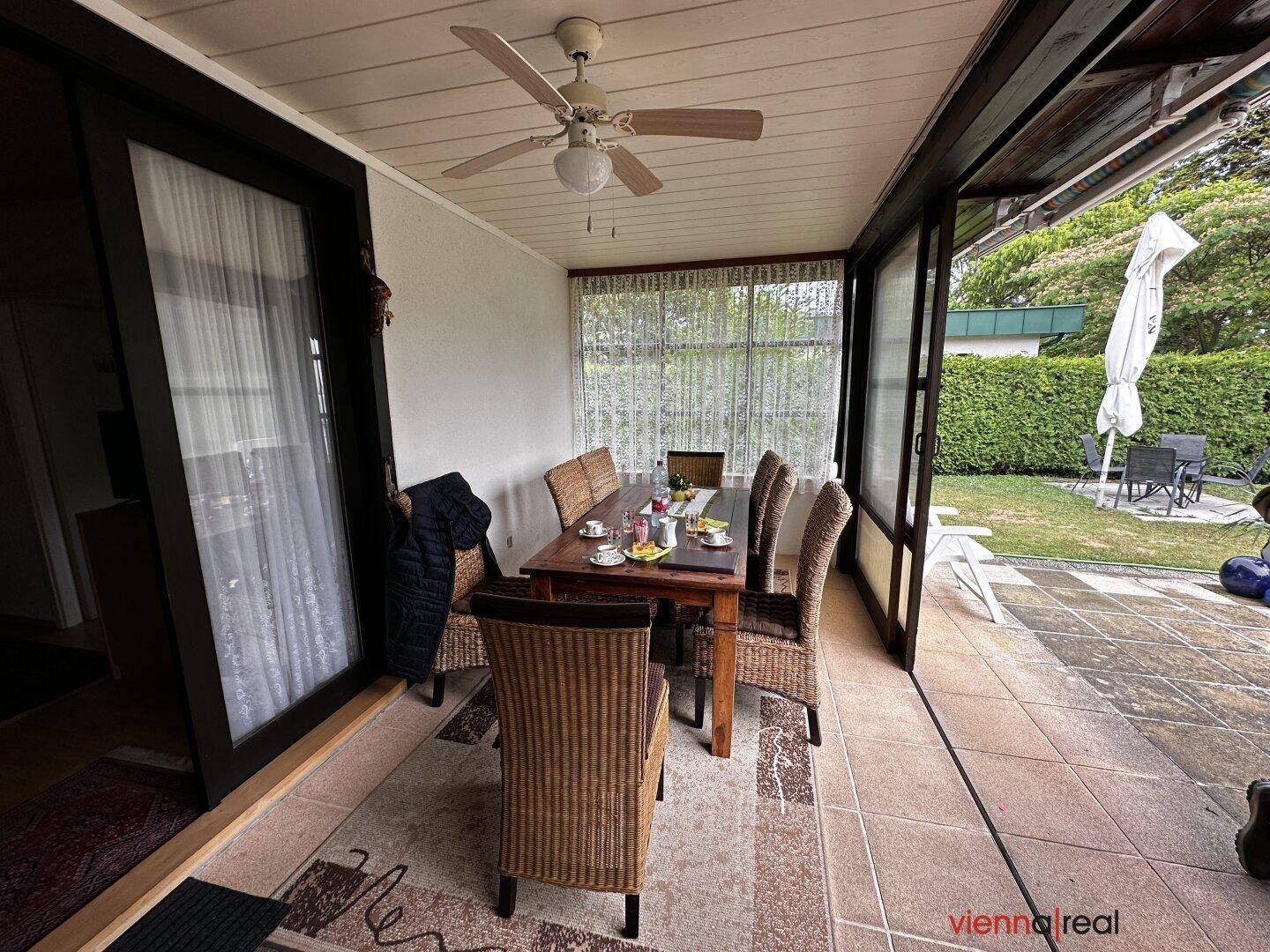 Überdachte Terrasse mit Esstisch und Deckenventilator, die als erweiterter Wohnbereich dient.