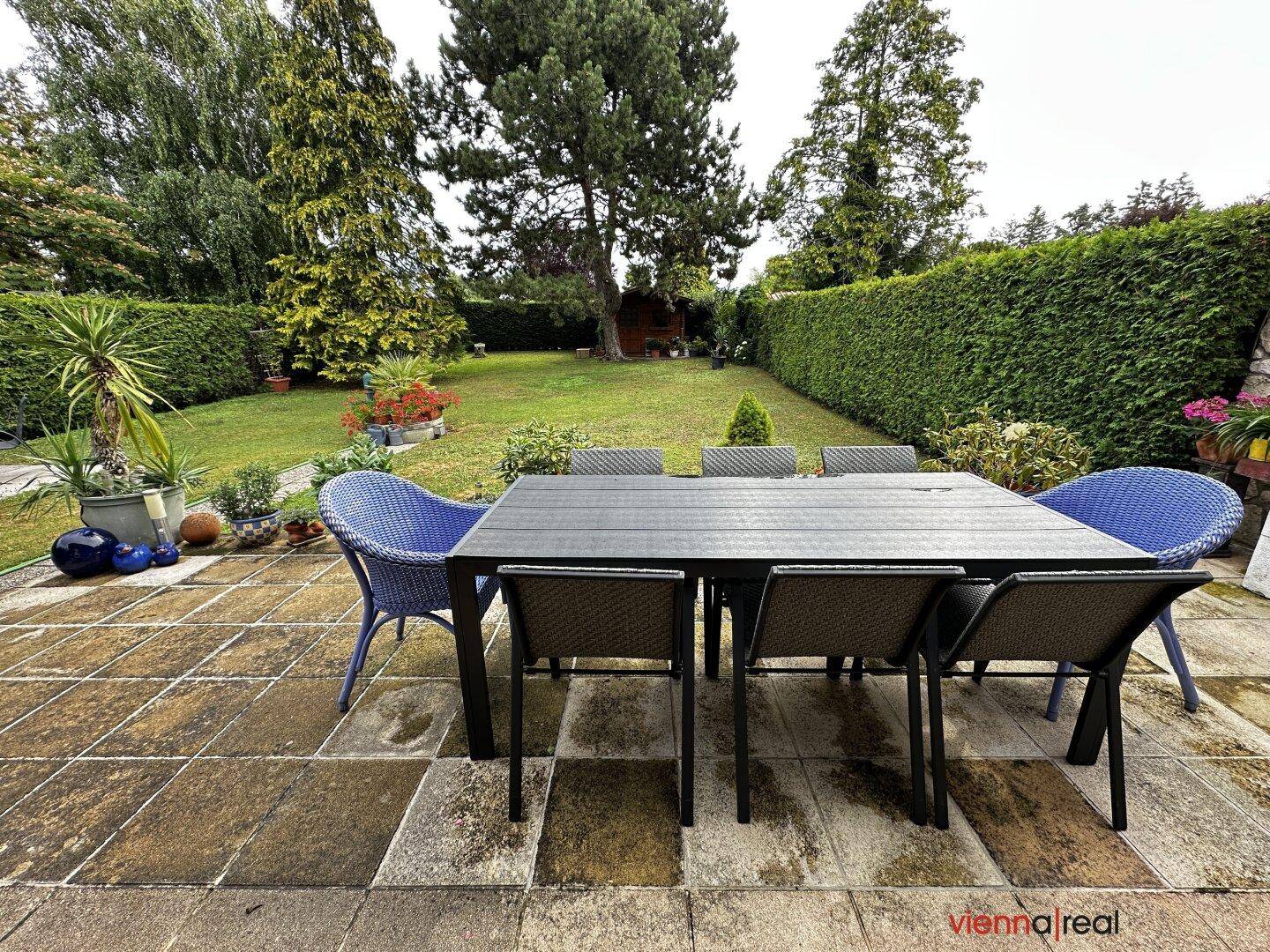 Geräumige Terrasse mit großem Esstisch und Stühlen, umgeben von einem gepflegten Garten.