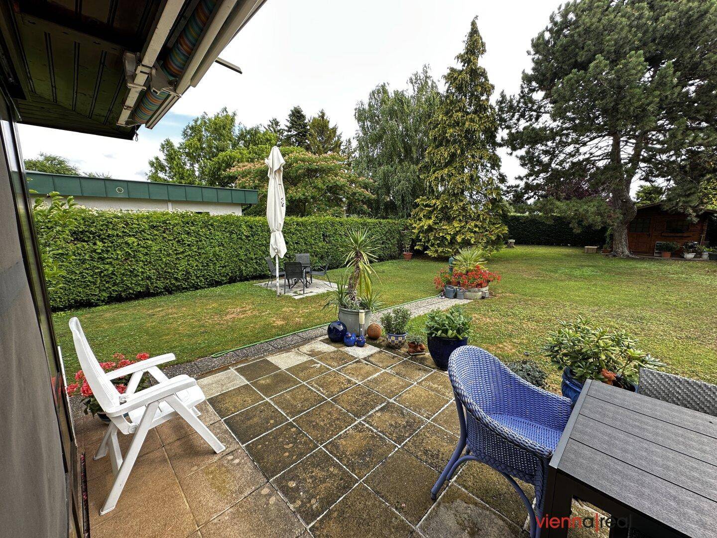 Terrasse mit Fliesenboden und Gartenmöbeln, angrenzend an eine große Rasenfläche.