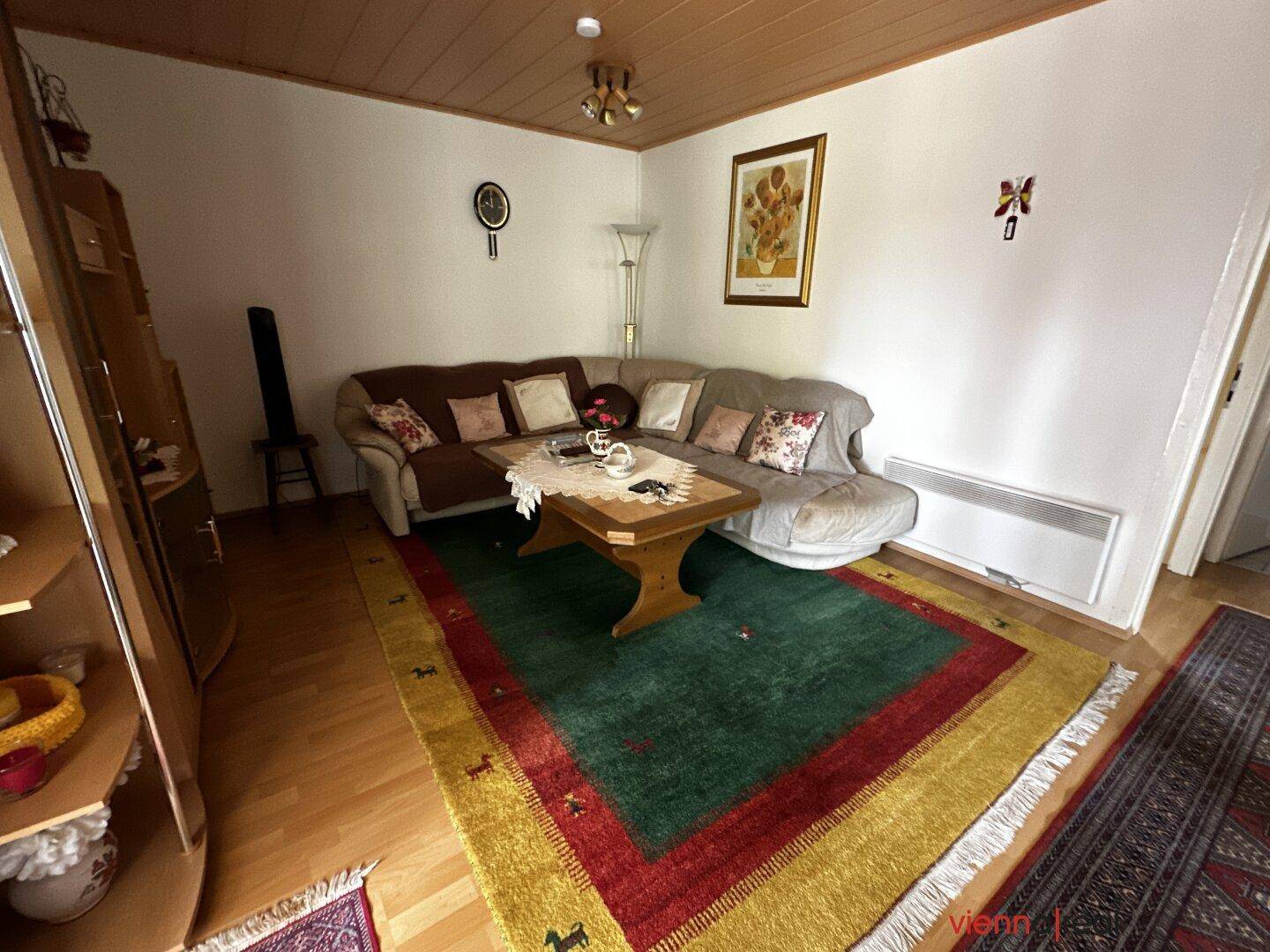 Gemütliches Wohnzimmer mit Ecksofa, Couchtisch und Holzboden, dekoriert mit bunten Teppichen.
