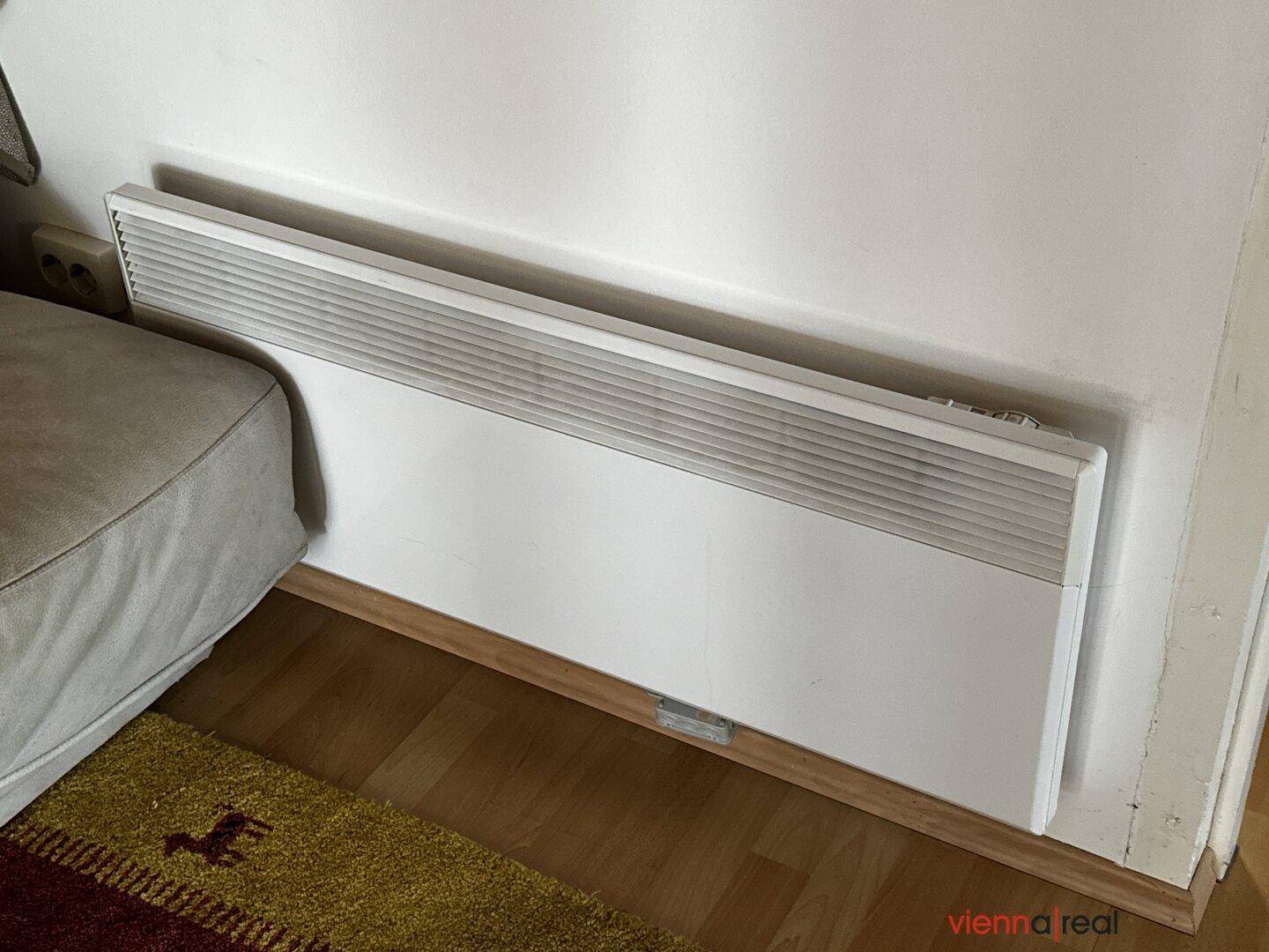 Nahaufnahme eines Heizkörpers an der Wand in einem Wohnbereich mit Holzboden.