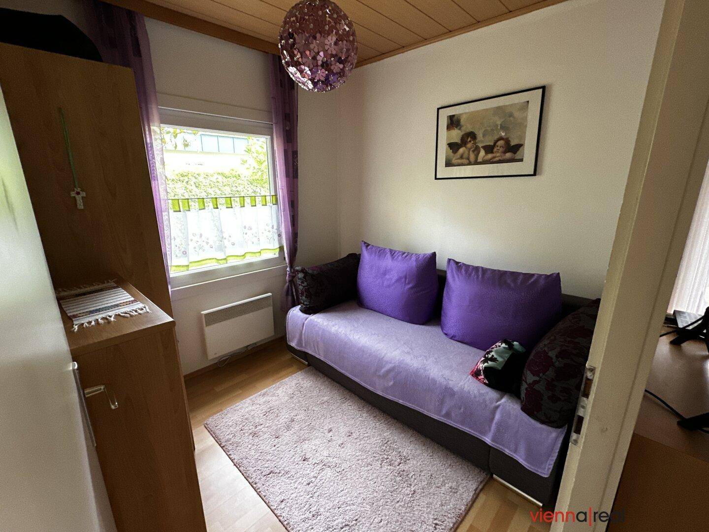 Kleines Schlafzimmer mit Einzelbett, lila Kissen und Vorhängen sowie Holzboden.