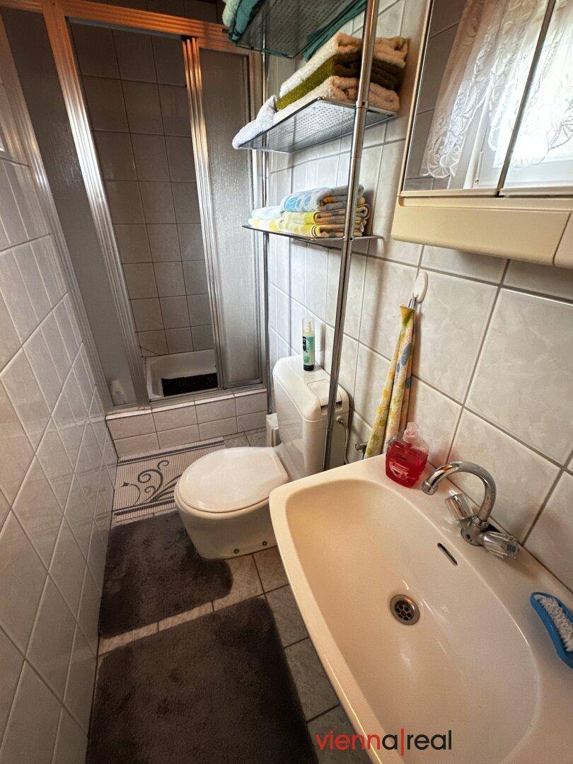 Kleines Badezimmer mit Dusche, WC und Waschbecken, gefliest in hellen Farbtönen.