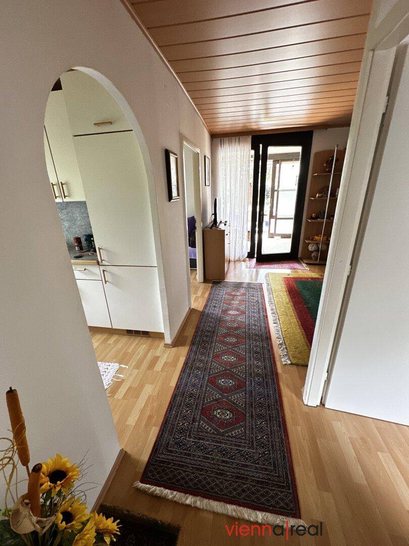 Heller Flur mit Holzboden, Teppichen und einem Bogen, der zur Küche führt.