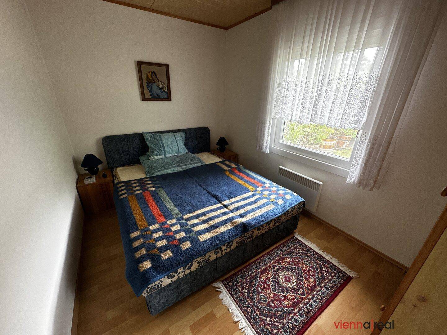 Schlafzimmer mit Doppelbett, Holzboden und einem Fenster mit Blick in den Garten.