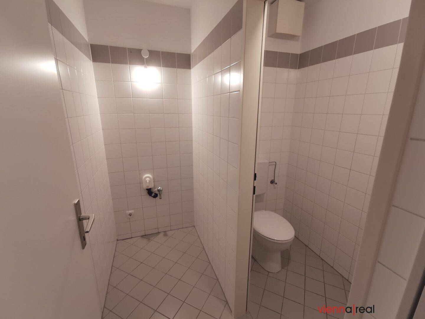 Separate Toilette mit weißen Wandfliesen und einem kleinen Fenster, das für Belüftung sorgt.