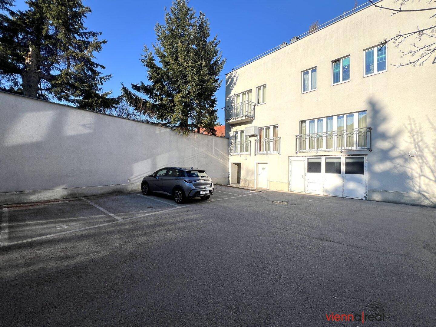 Außenparkplatz mit einem geparkten Auto vor einem modernen Gebäude unter blauem Himmel.