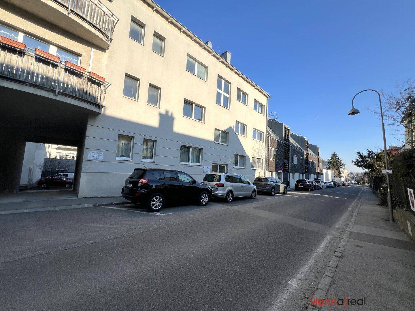 Ruhige Wohnstraße mit geparkten Autos und Gebäuden auf beiden Seiten unter blauem Himmel.