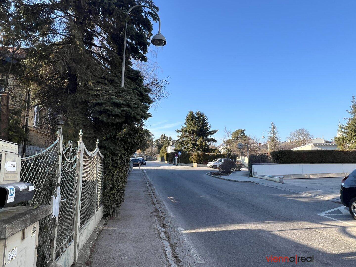 Ruhige Wohnstraße mit Bäumen und einem Zaun, die eine angenehme Umgebung zeigt.