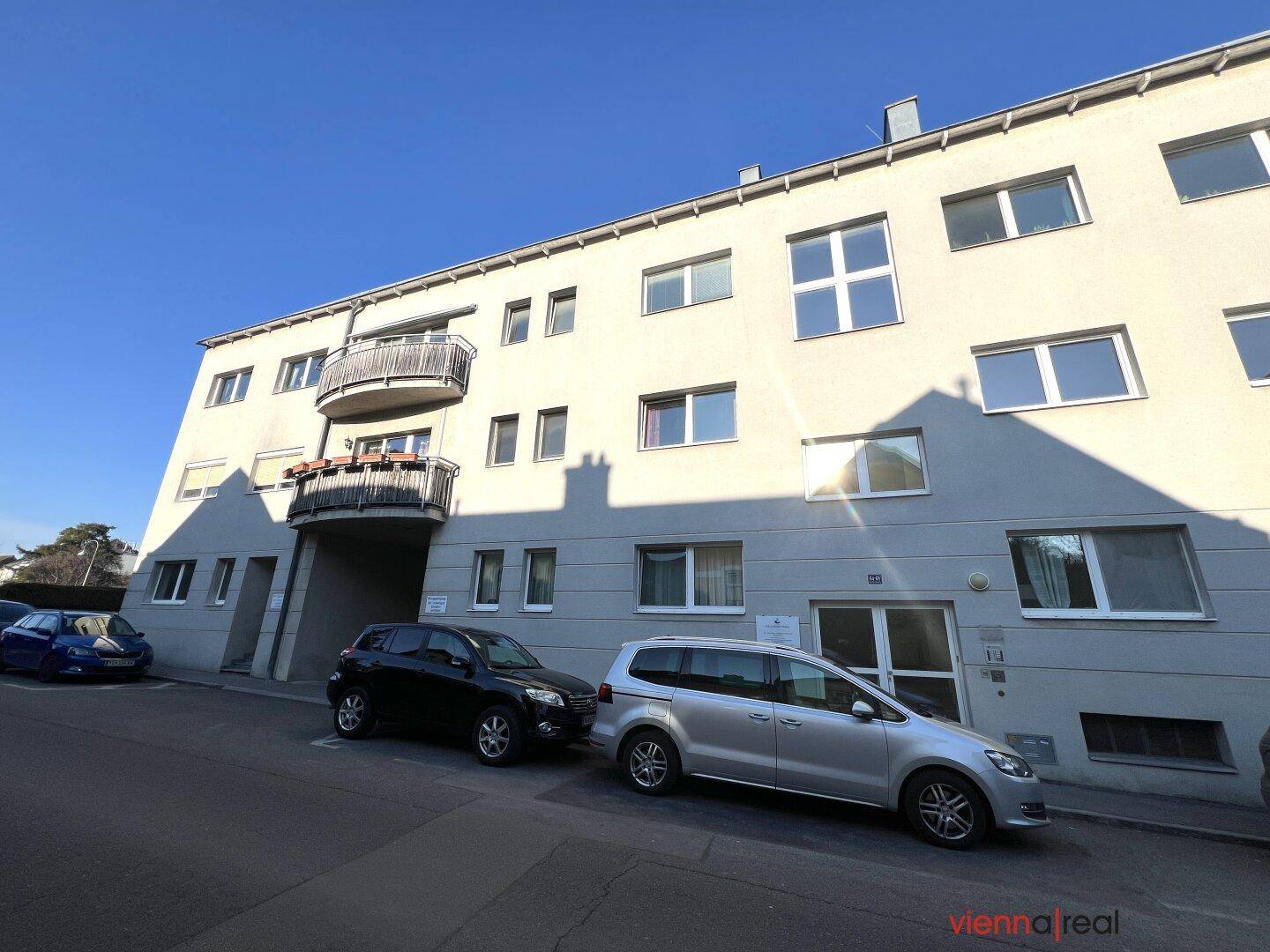 Ansicht eines Mehrfamilienhauses mit Balkonen und geparkten Autos auf der Straße.