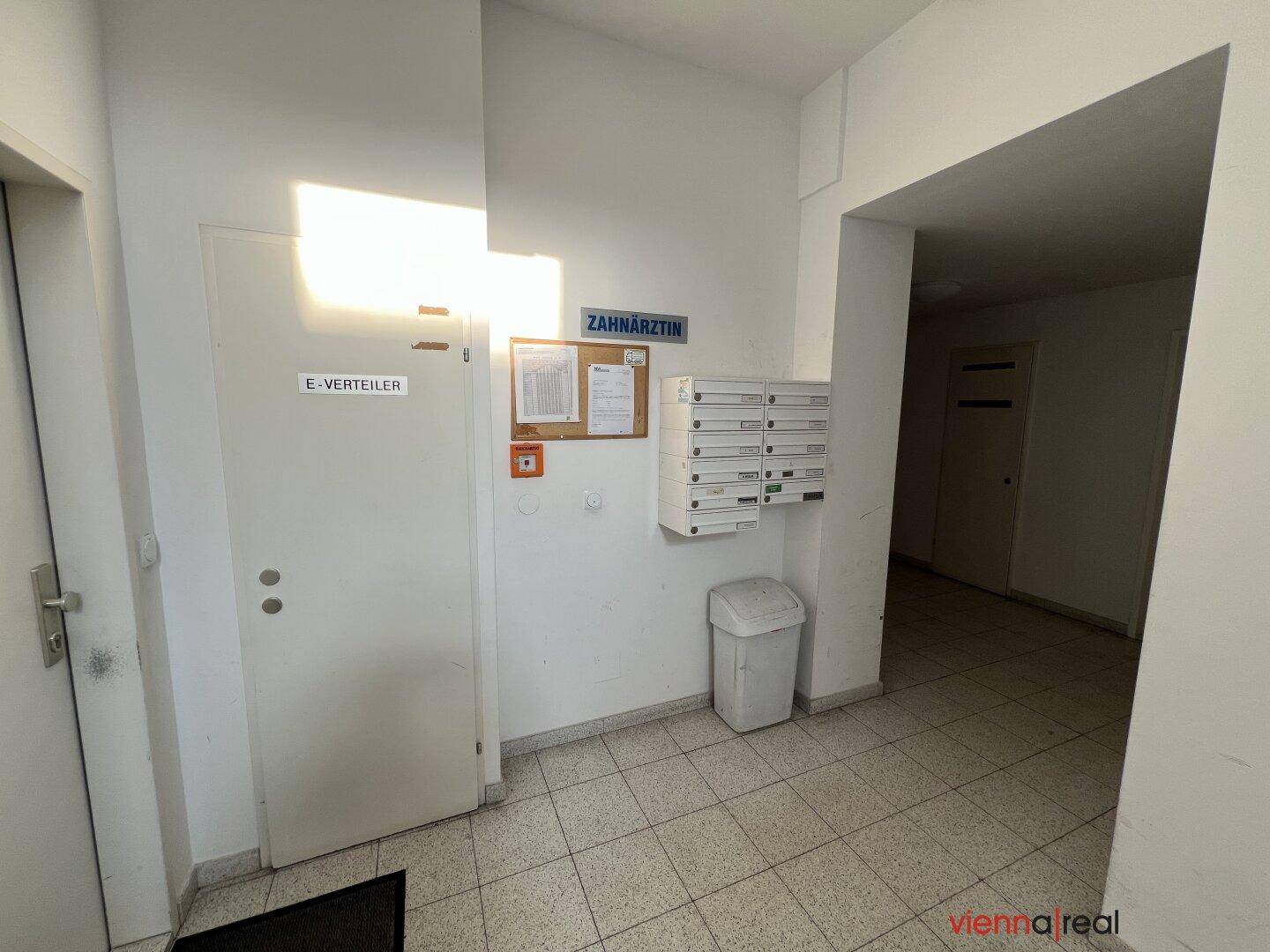 Eingangsbereich eines Mehrfamilienhauses mit Briefkästen, Hinweistafeln und einer Tür.