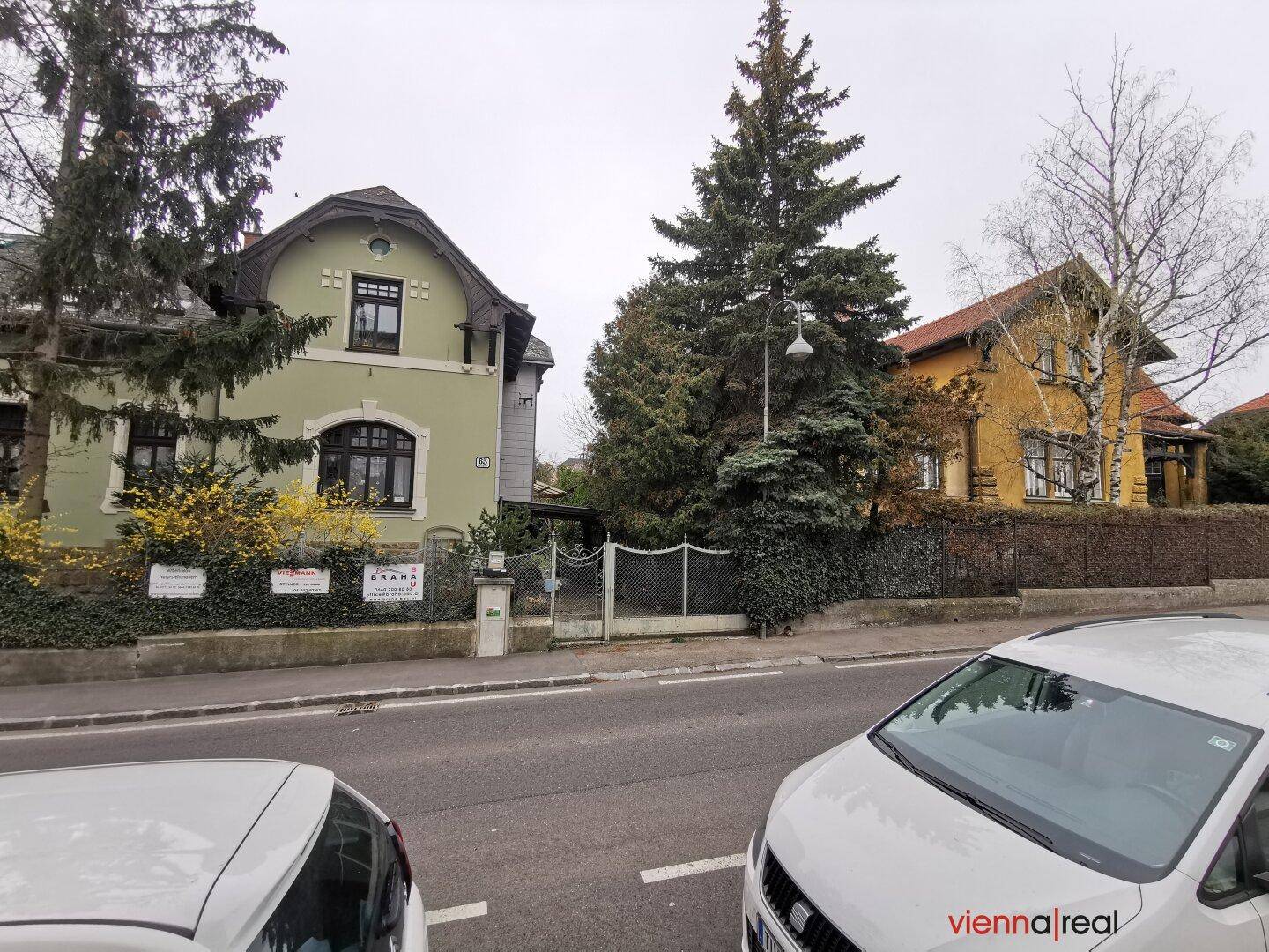 Ansicht einer ruhigen Wohnstraße mit traditionellen Häusern und geparkten Autos unter bewölktem Himmel.
