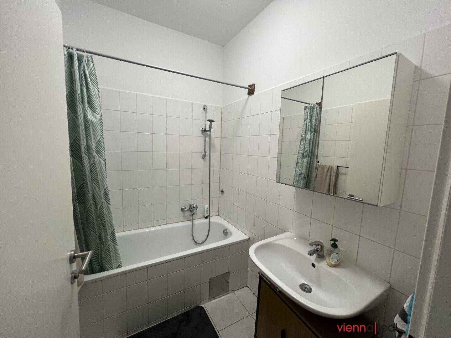 Helles Badezimmer mit Badewanne, Duschvorhang und Spiegelschrank.