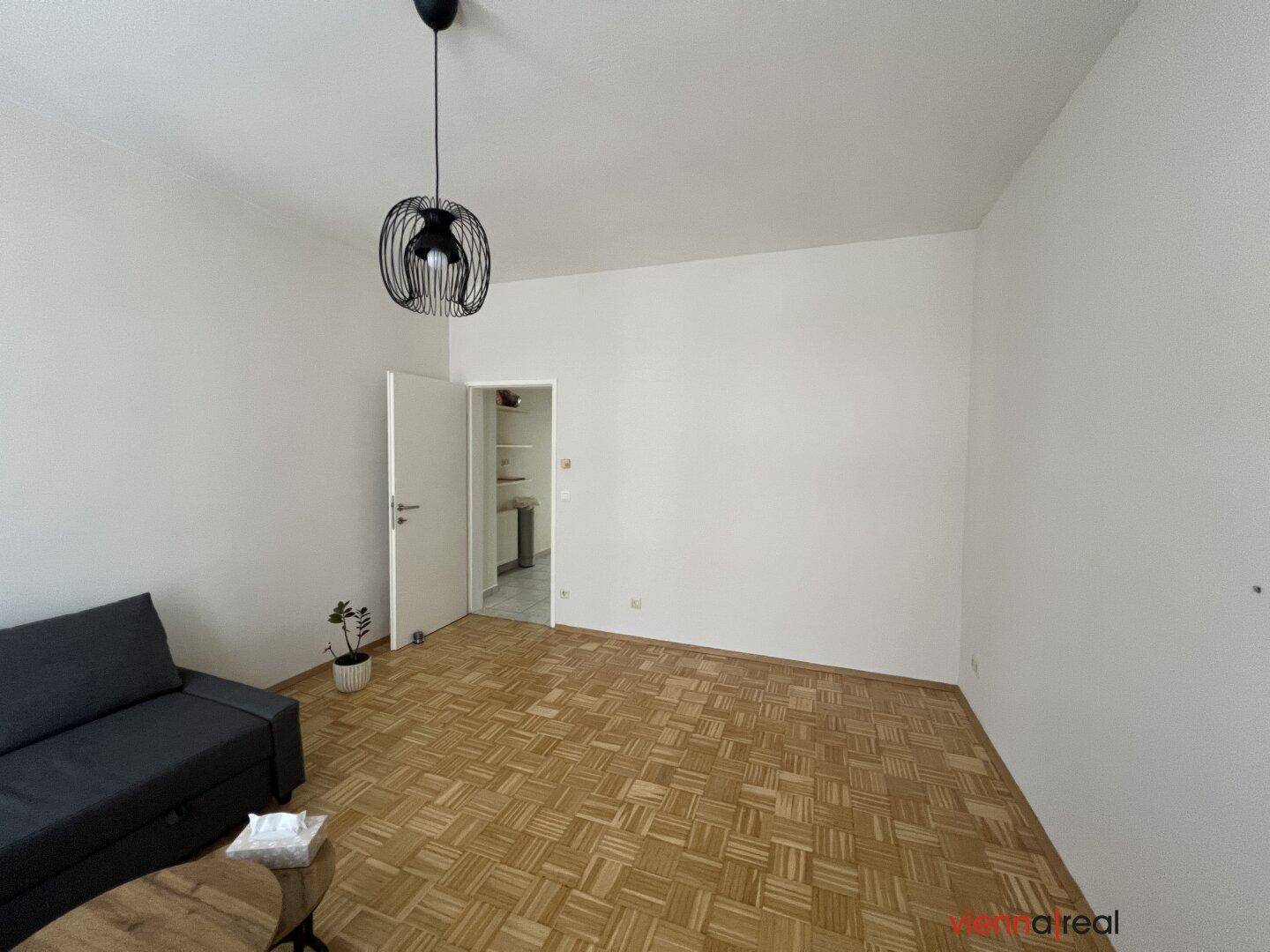 Geräumiges Wohnzimmer mit hellem Parkettboden und schlichtem, modernem Design.