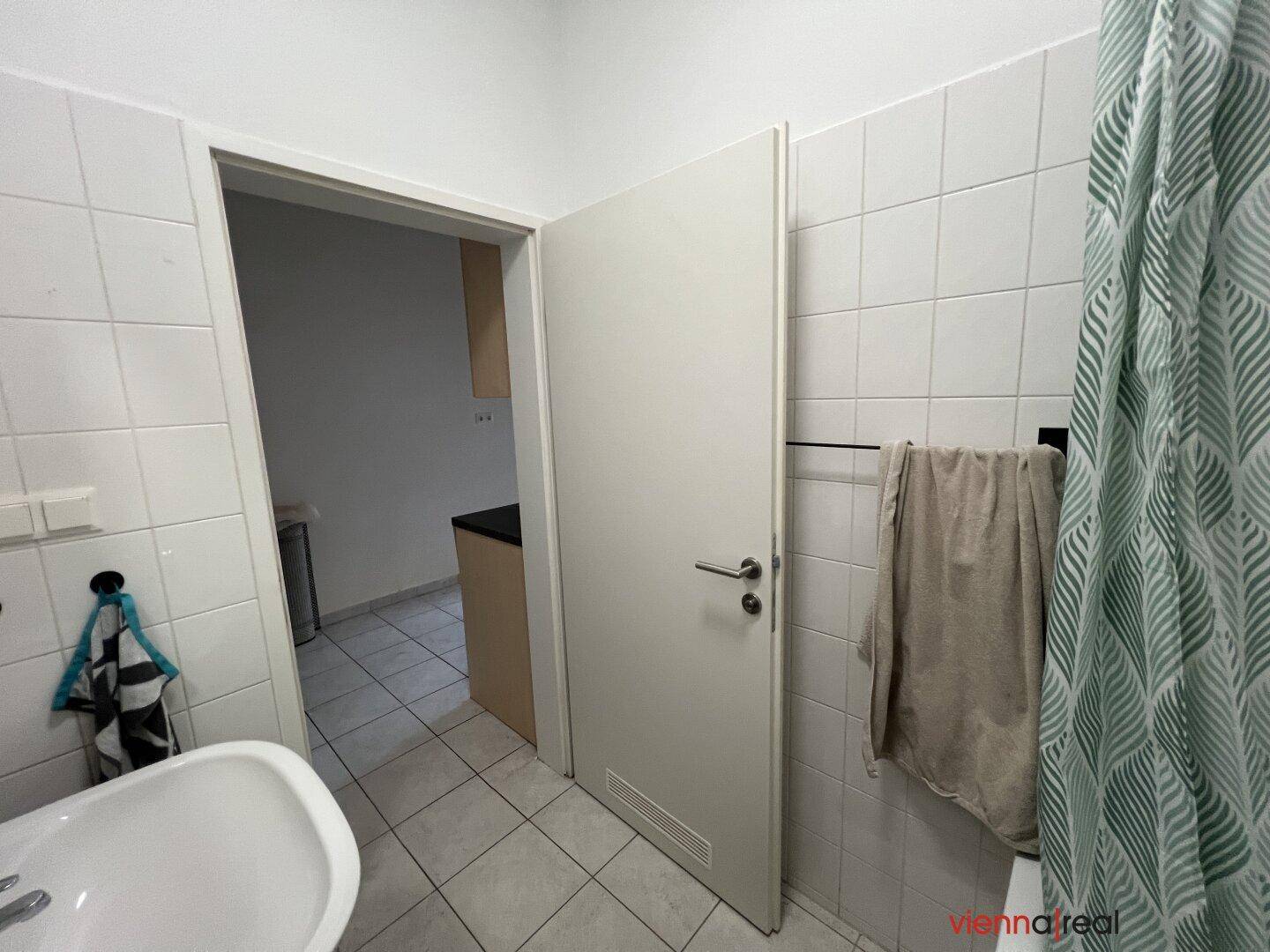Badezimmer mit Fliesen und Zugang zur Küche, ausgestattet mit Badewanne und Waschbecken.