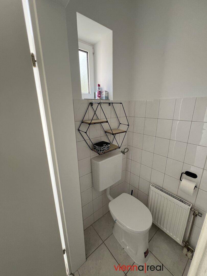Separates WC mit Fenster, Fliesen und Heizkörper, ausgestattet mit Wandregal.