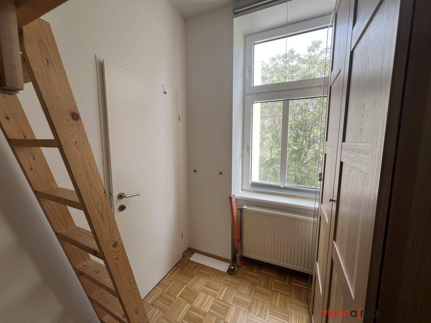 Helles Schlafzimmer mit Fenster, Heizkörper und Holzschrank, ideal für ein Kinderzimmer.