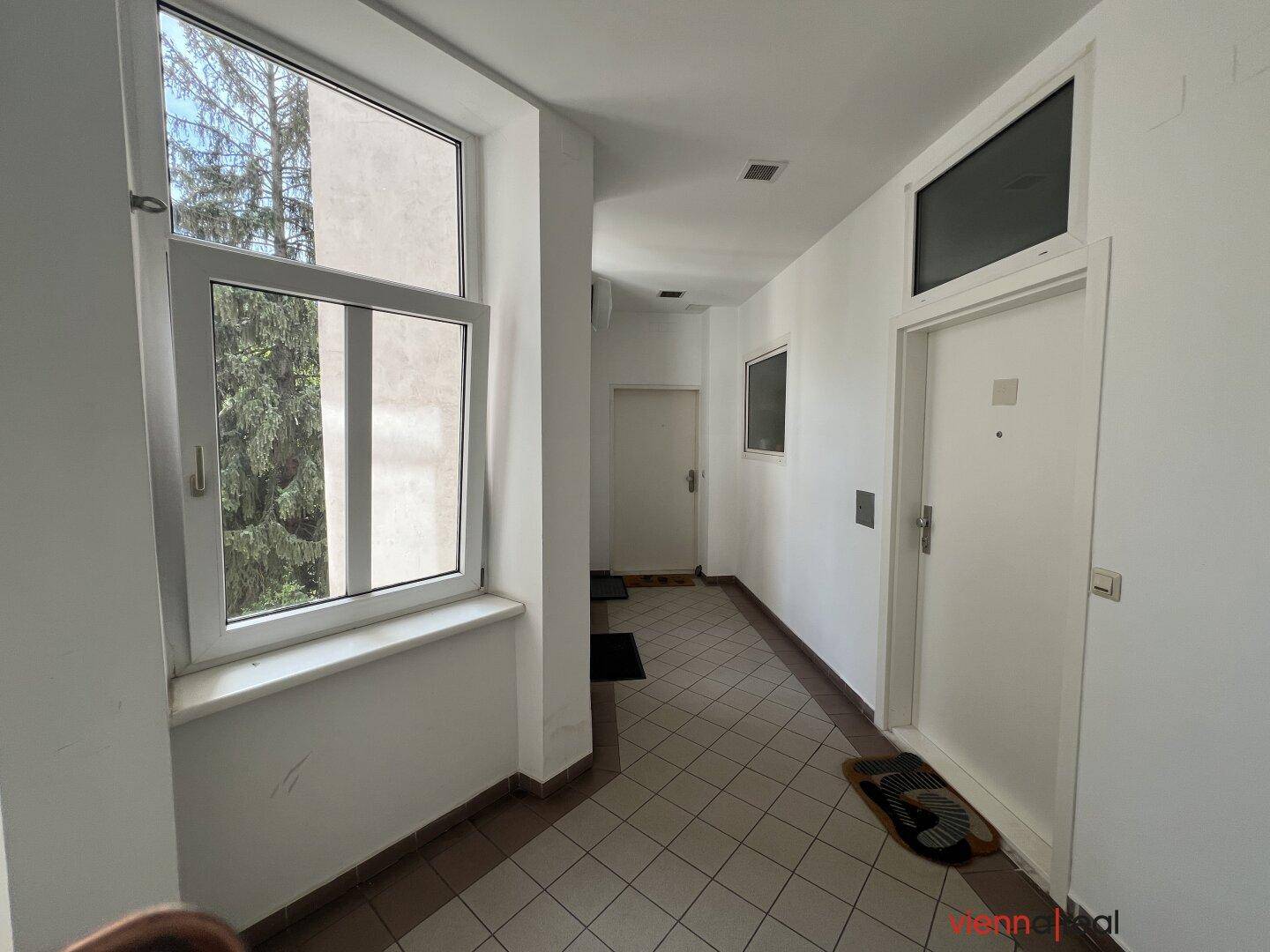 Geräumiger Eingangsbereich mit mehreren Türen und viel Tageslicht durch große Fenster.