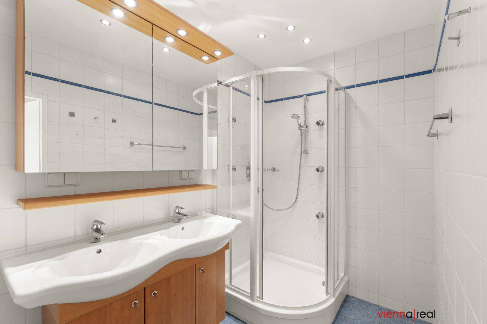 Modernes Badezimmer mit Eckdusche, Doppelwaschbecken und weißen Fliesen mit blauen Akzenten.