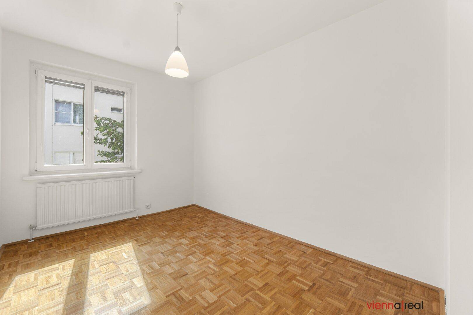 Helles Zimmer mit Parkettboden und weiß gestrichenen Wänden, mit Blick auf die umliegenden Gebäude.