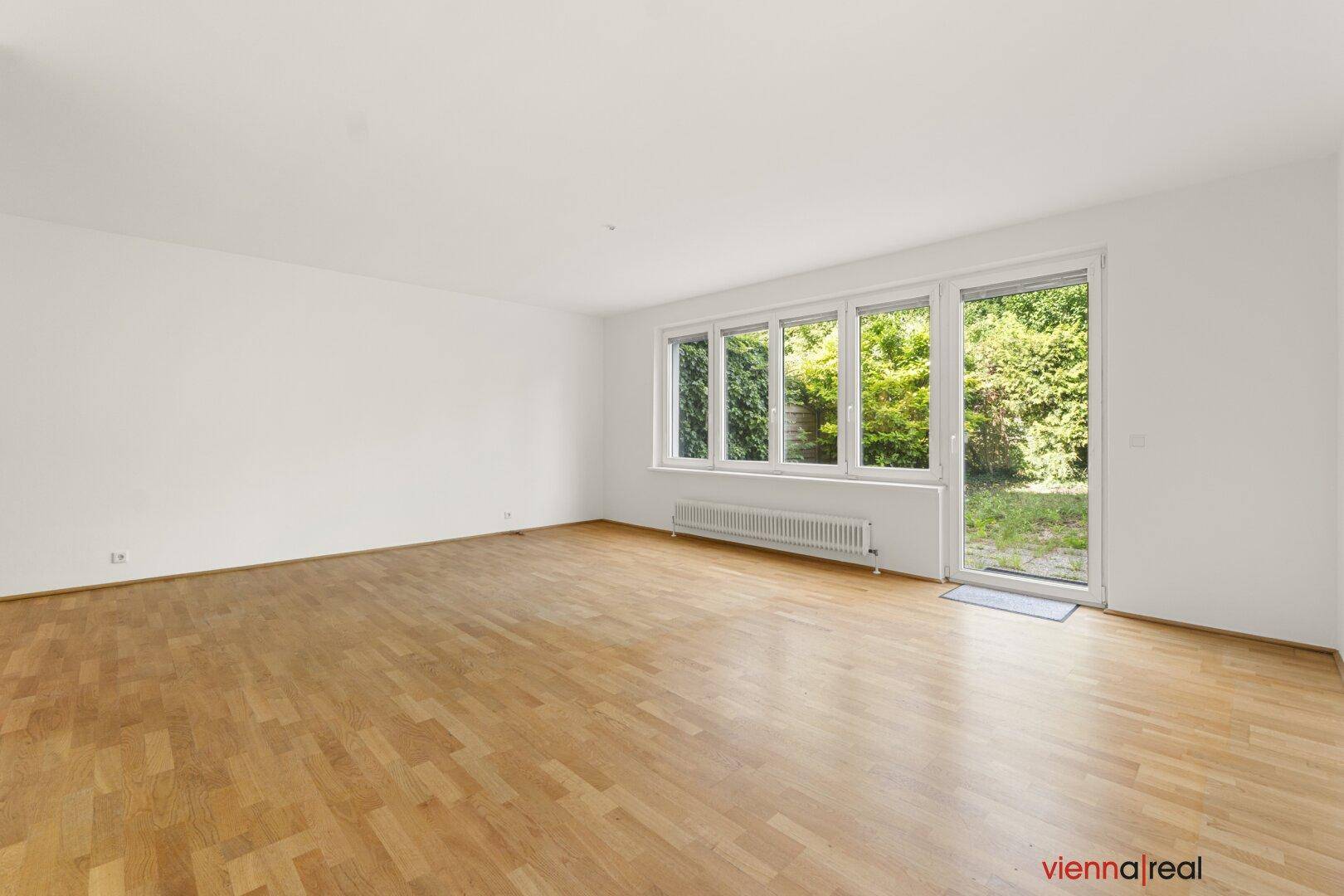 Geräumiges Wohnzimmer mit Parkettboden und großen Fenstern, die viel Licht hereinlassen und Zugang zum Garten bieten.