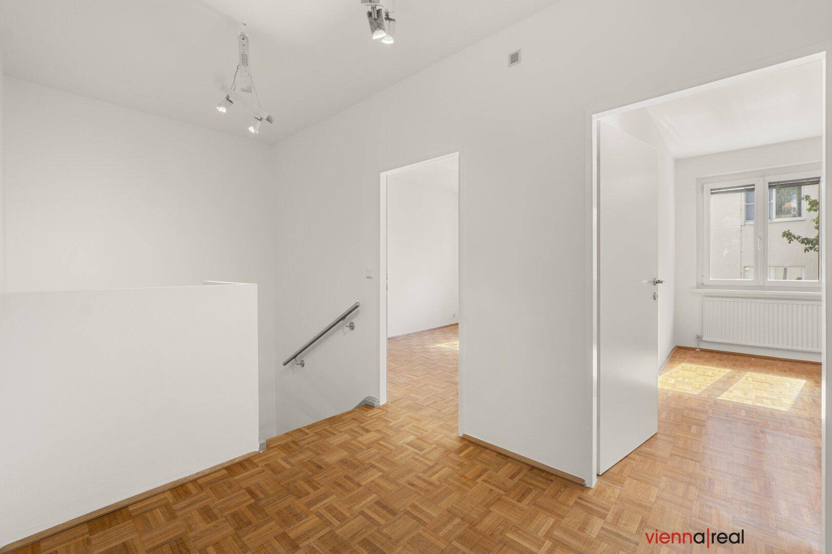 Heller Flur mit Parkettboden und Zugang zu weiteren Räumen, inklusive einer modernen Treppe.